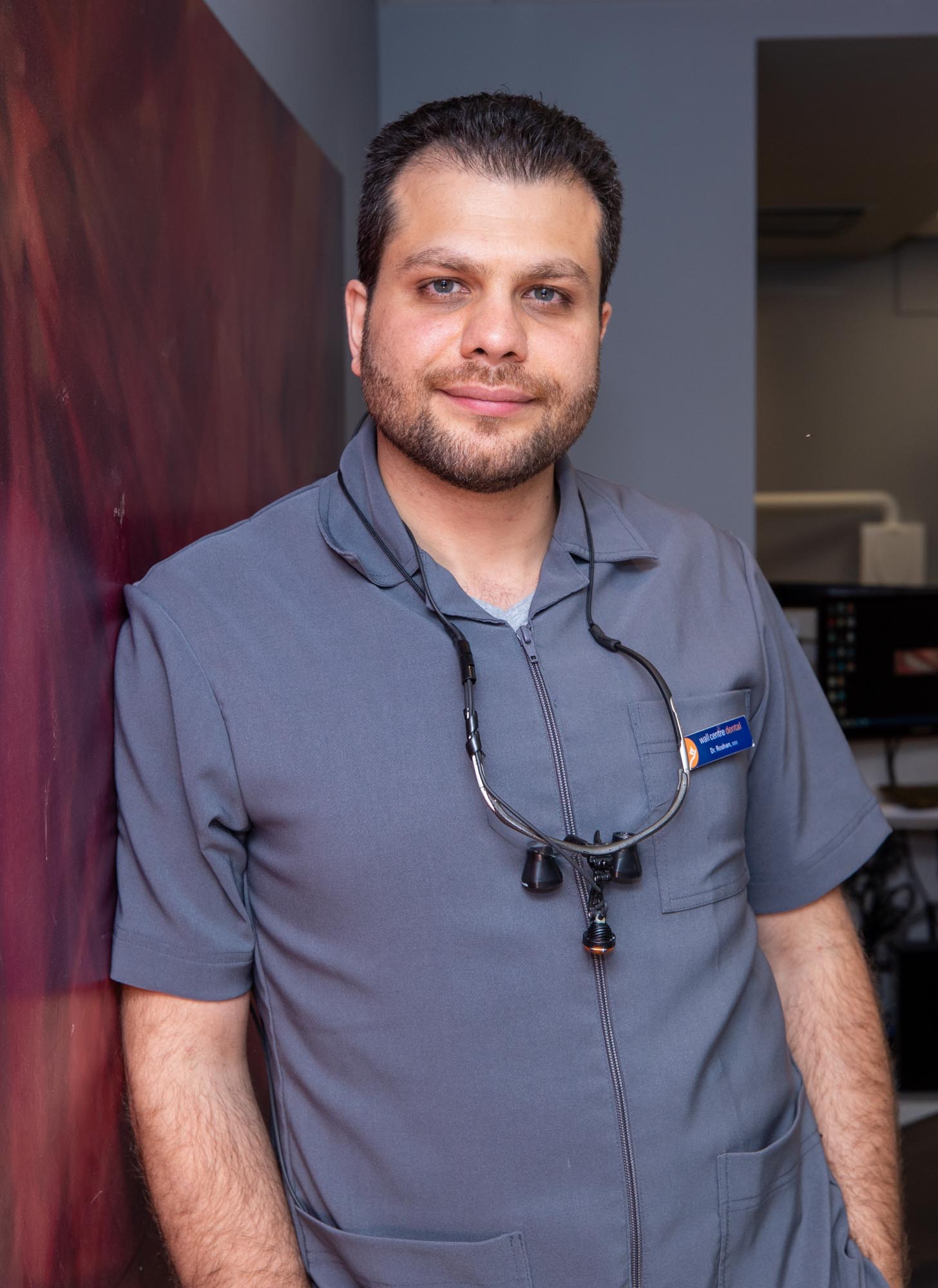 Dr. Parviz Roshanzamir leaning against a wall smiling with the office in the background.
