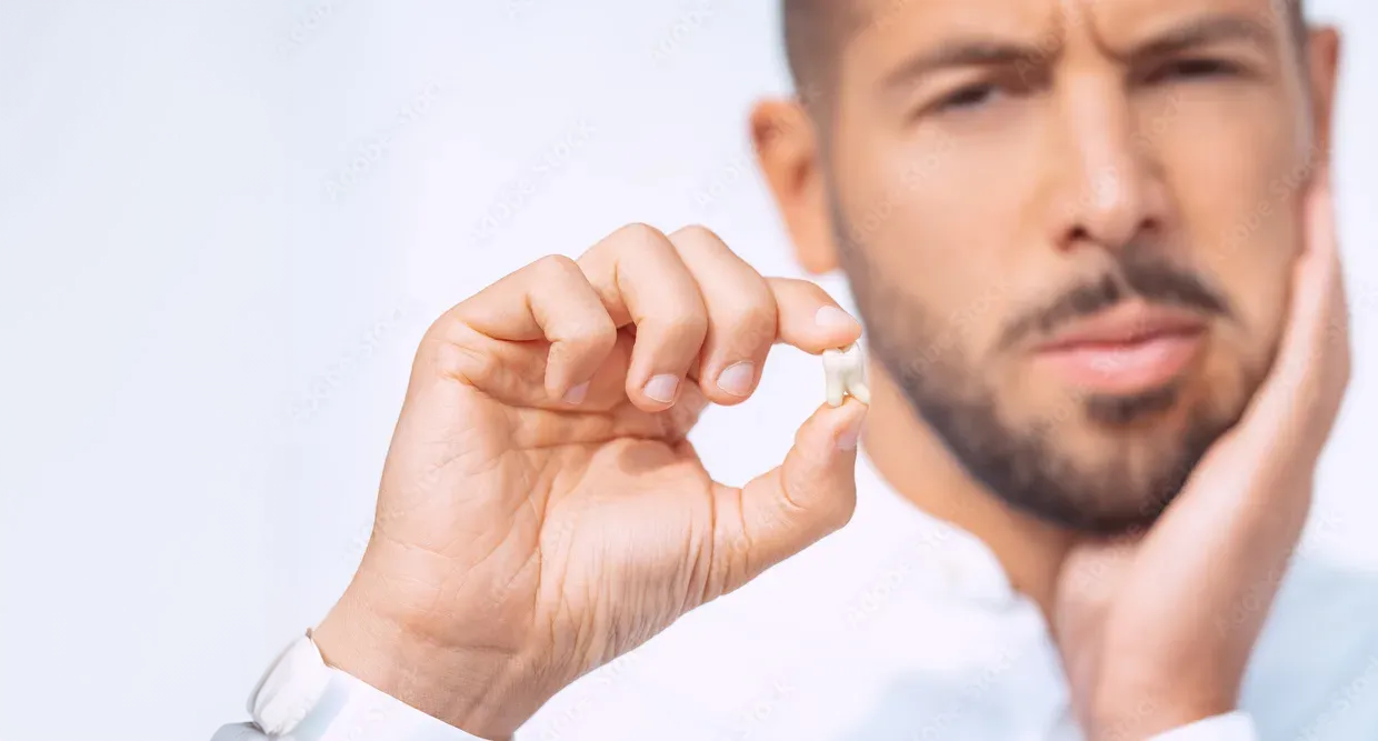 Man holding up a tooth in one hand and his other hand is on his jaw showing it hurts.